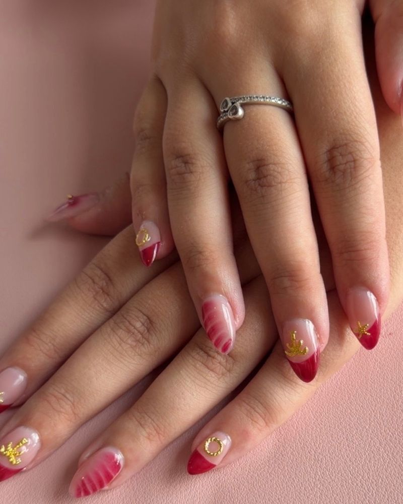 Almond nails with red French tips, blush art and gold charms